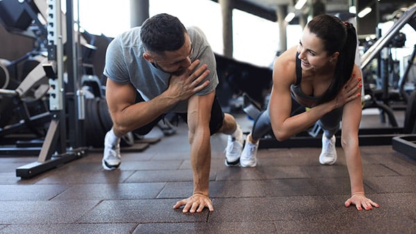 Un homme et une femme font du gainage dynamique à la salle de musculation.