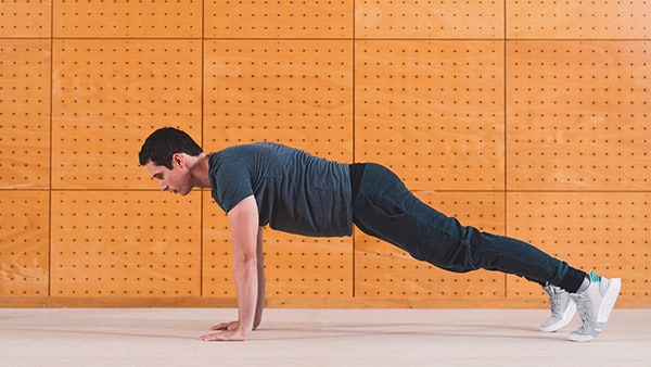 A man is doing the plank in a high position, arms outstretched.