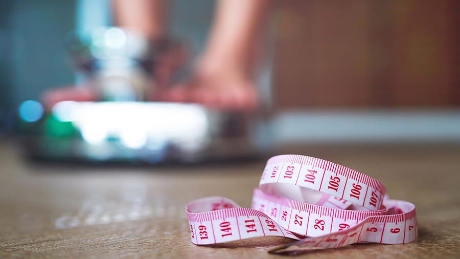 Une personne se pèse sur une balance, avec un mètre à proximité