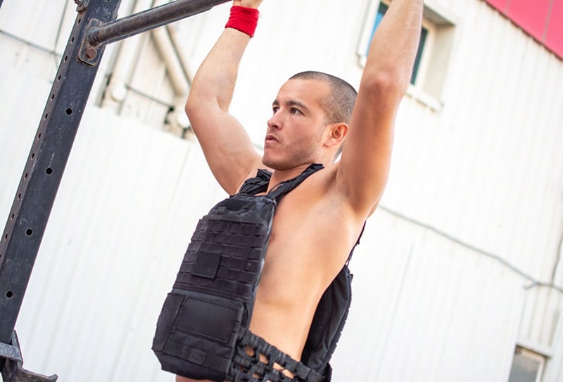 A man does a pull with a weighted vest on his back.