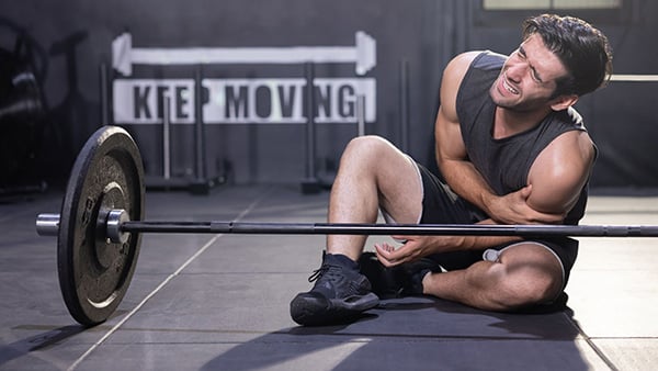 Un sportif qui souffre du bras devant une barre de musculation.