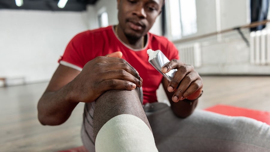 A sportsman puts ointment on his knee.