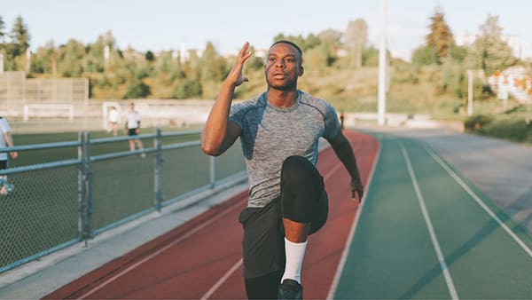 Un sportif fait des montées de genoux pour s'échauffer sur une piste d'athlétisme.