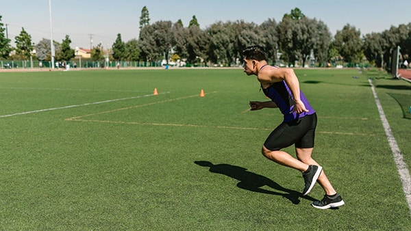 Un sportif court le Luc Léger sur un terrain de sport en gazon synthétique.