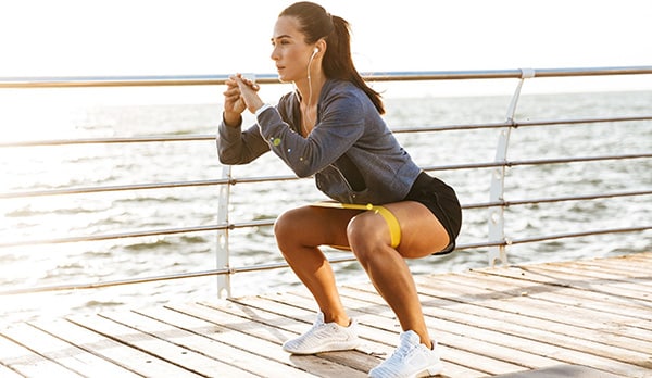 Une femme avec des écouteurs réalise des squats au poids du corps en bord de mer.