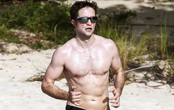 The actor Robert Pattinson jogs shirtless on the beach.