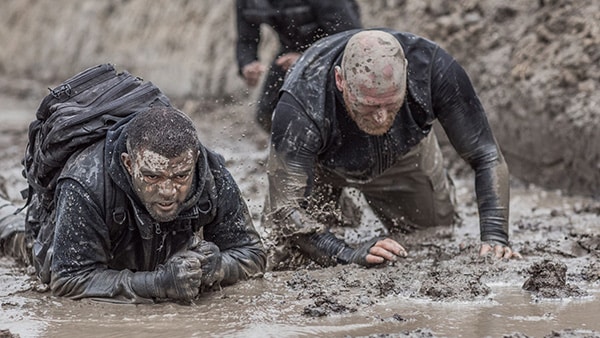 Military personnel lying in the mud during an obstacle course.