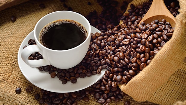 A cup of coffee with an open bag of coffee beans.