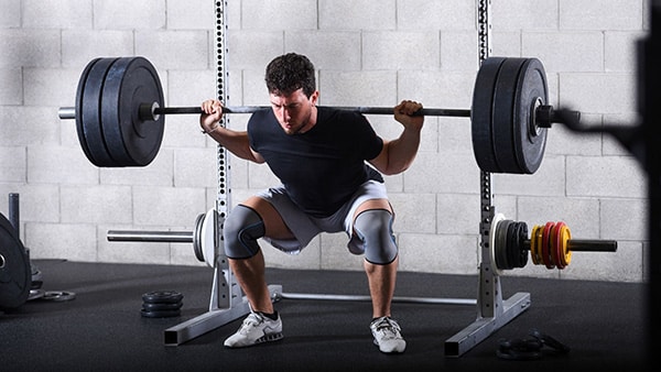 Un athlète effectue l'exercice du squat avec une barre de musculation dans une salle de sport.