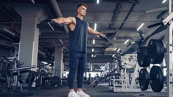 An athletic man performs lateral lifts at the weight room.