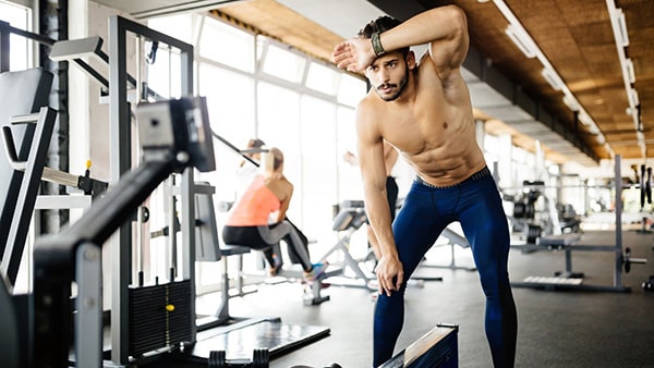 Un sportif torse nu montrant des signes de fatigue à la salle de musculation.