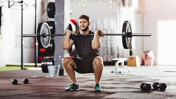 A man is doing the squat exercise in a gym.