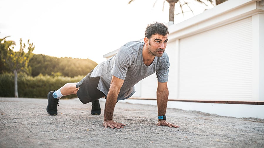 A man in shorts and a t-shirt performs push-ups as part of a beginner HIIT circuit.