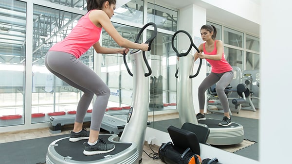 A woman works out in a gym on a vibrating platform