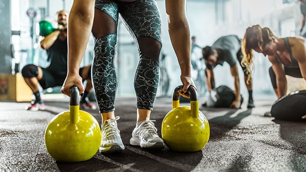 An athlete is about to lift 2 yellow kettlebells in a fitness room.