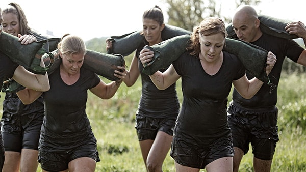 4 women and 1 man walk with sandbags on their backs.