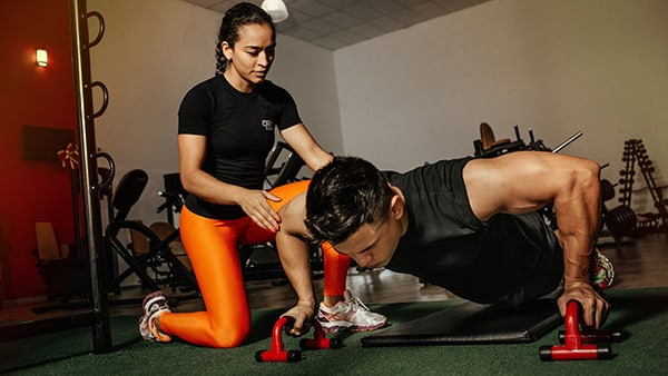 Un homme effectue des pompes avec des poignées push-up sous le regard d'une coach sportive.