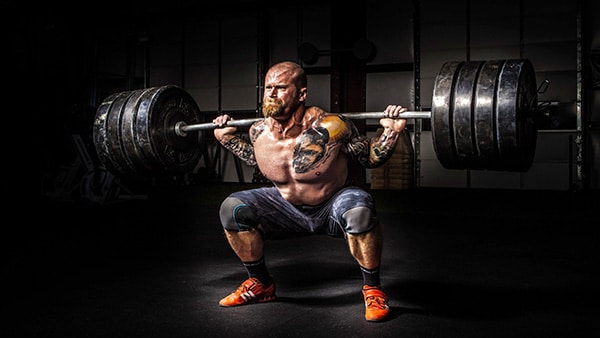 A shirtless man does squats with heavy loads.