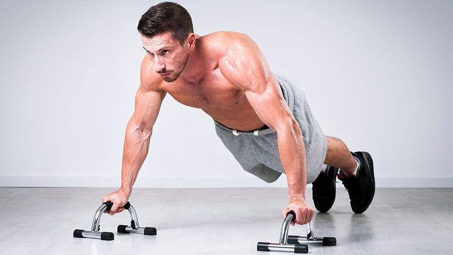 Un homme torse nu utilise des poignées de pompes pour faire de la musculation.