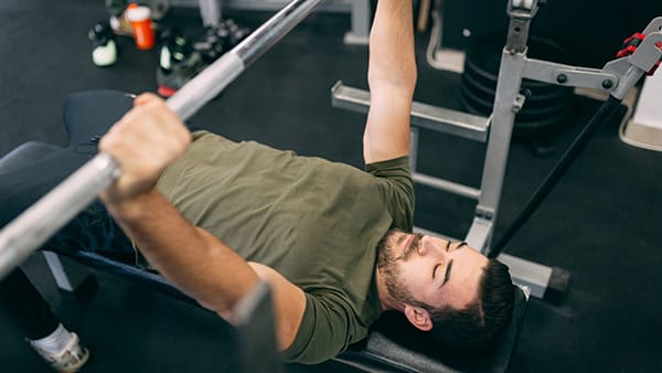 A man performs the bench press exercise in a weight room.