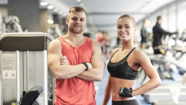 2 sports coaches (1 man and 1 woman) in a fitness and weight room.