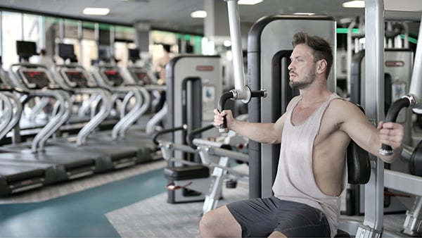 A man performs a pectoral exercise in a gym.