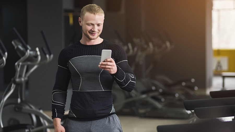 A man in a gym checks his smartphone for the best weight training application.