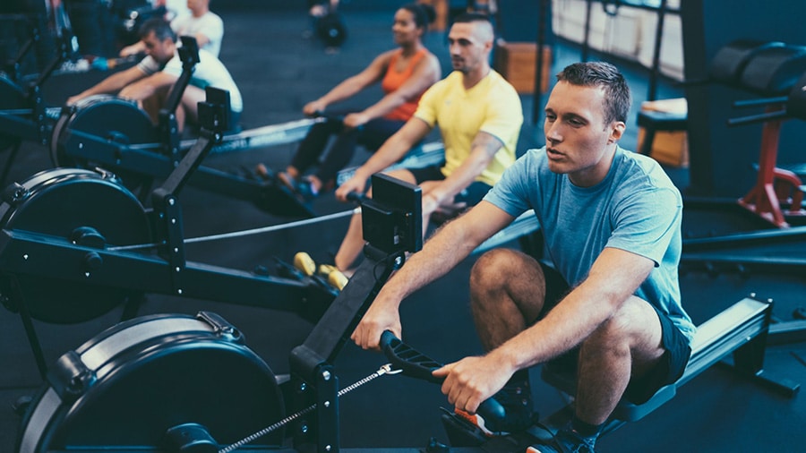 Athletes train on rowing machines in a gym.