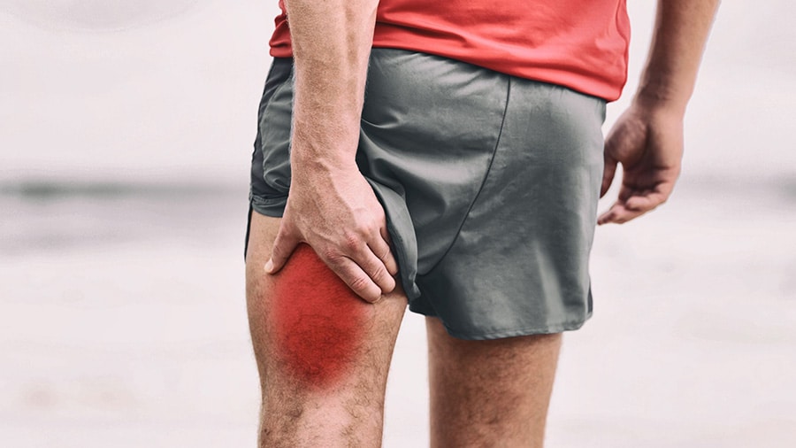 An athlete in shorts is holding the back of his left thigh following an injury such as a muscle strain.