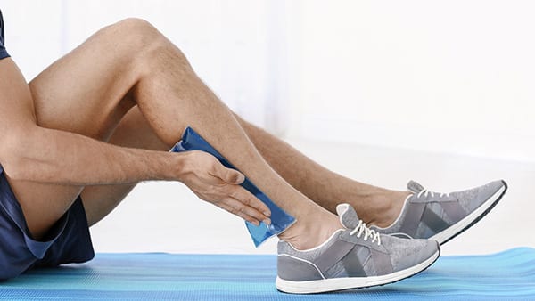 A man applies an ice pack to his right calf.