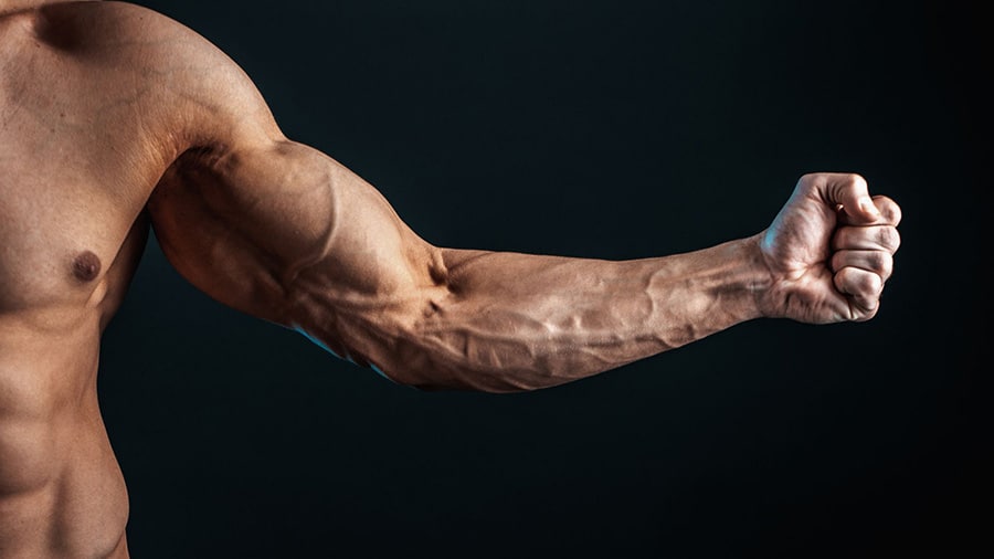 A shirtless man clenches his fist and contracts his biceps to see his arm vein appear.