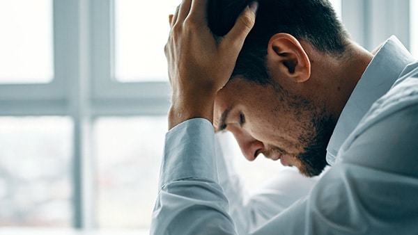 Un homme stressé se tient la tête dans les mains.