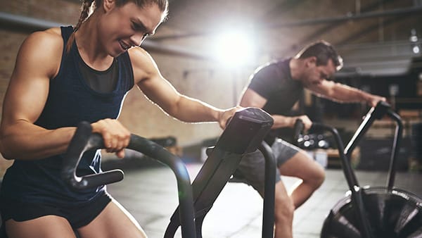 Un homme et une femme font du HIIT cardio sur un assault bike.