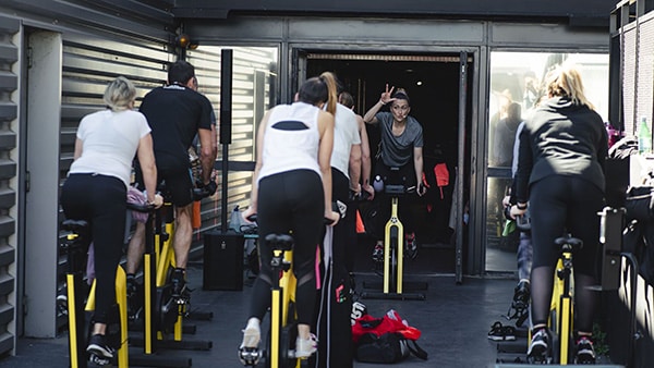 Une coach sportive encadre un cours collectif de RPM avec de nombreux participants.