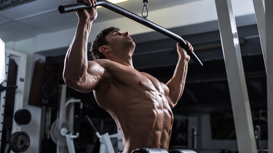 A torsoed man doing a weight training exercise in a gym (vertical pull)