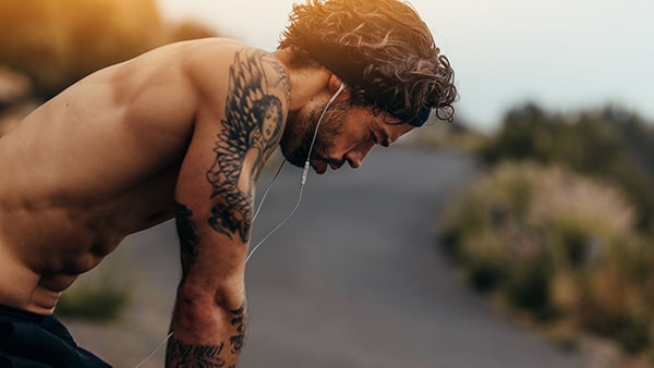 Un sportif torse nu portant des écouteurs est penché vers l'avant, mains sur les genoux.