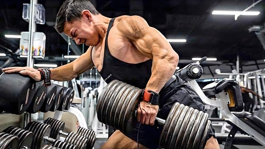 Le bodybuilder Tristyn Lee en train d'effectuer un exercice de musculation avec un haltère dans une salle de sport.