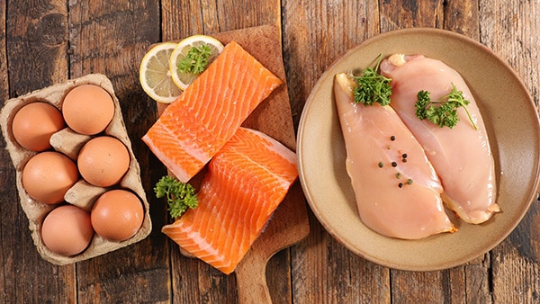 Protein-rich foods laid out on a table: eggs, salmon and chicken breast.