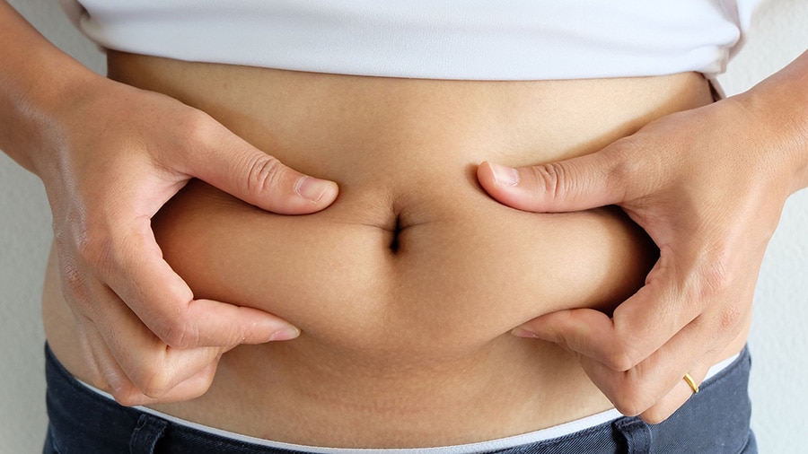 A person holds his belly fat between his two hands and wonders how to lose belly fat.