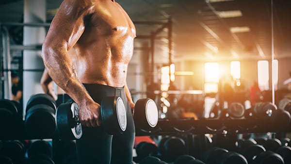 A shirtless man works out with dumbbells in his hands.