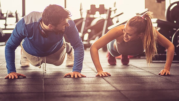 A man and a woman are doing the push-up exercise in a gym.