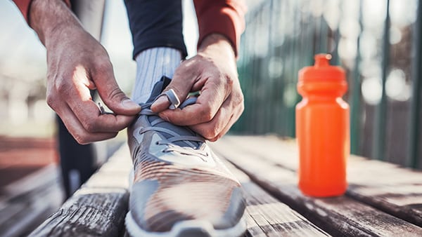 Un homme fait les lacets de ses chaussures de sport sur un banc, avec une gourde placée à côté.