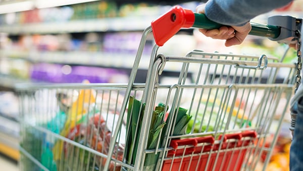 A person pushes a cart full of food while shopping in a supermarket.