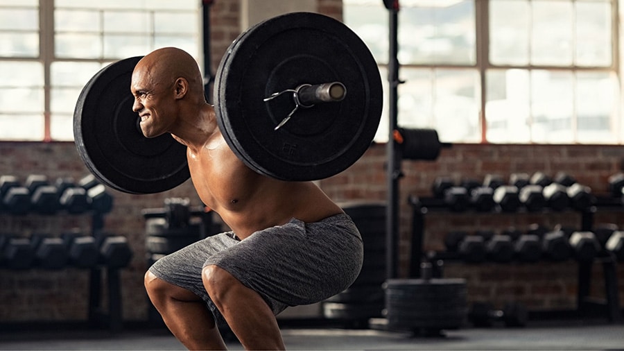 A shirtless man uses the rest pause technique on the squat exercise in a gym.