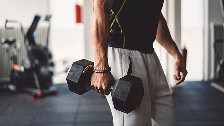 A man stands holding a dumbbell in his right hand in a weight room.