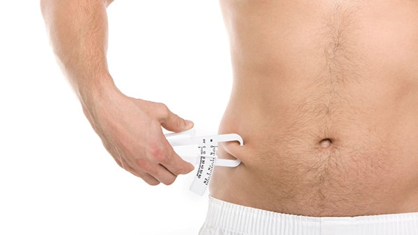 A shirtless man measures his belly fat with a skinfold tool.