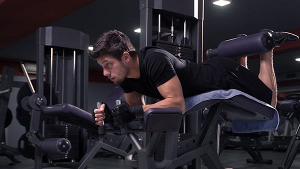 A man performs the leg curl exercise lying down in a weight room to strengthen his ischios.