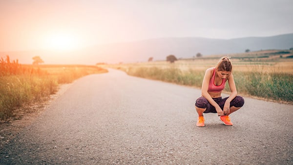 An athletic woman is crouching on a path in the wilderness during a running trip.