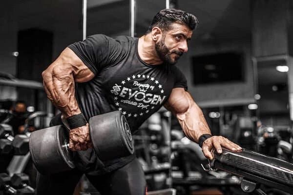 Hadi Choopan performs a pull-up exercise with a dumbbell in his right hand in a weight room.