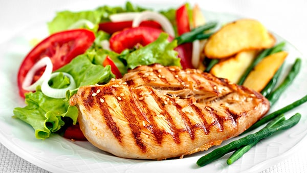 An athlete's meal on a plate with grilled chicken, salad, tomato and potato.